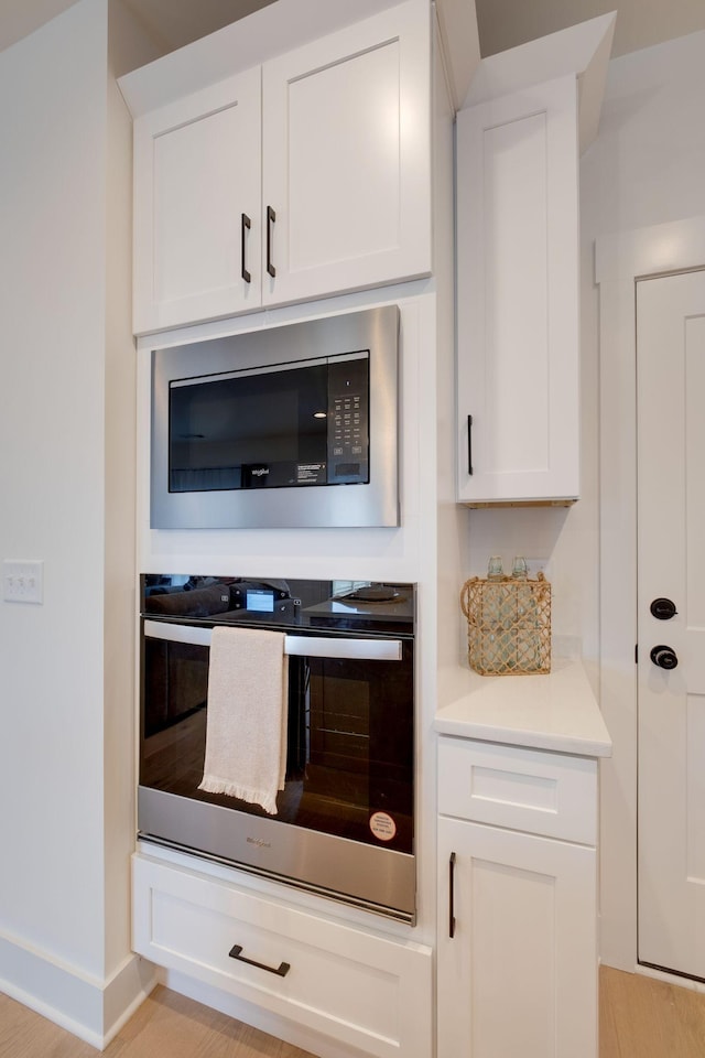 kitchen with baseboards, oven, light countertops, white cabinetry, and stainless steel microwave