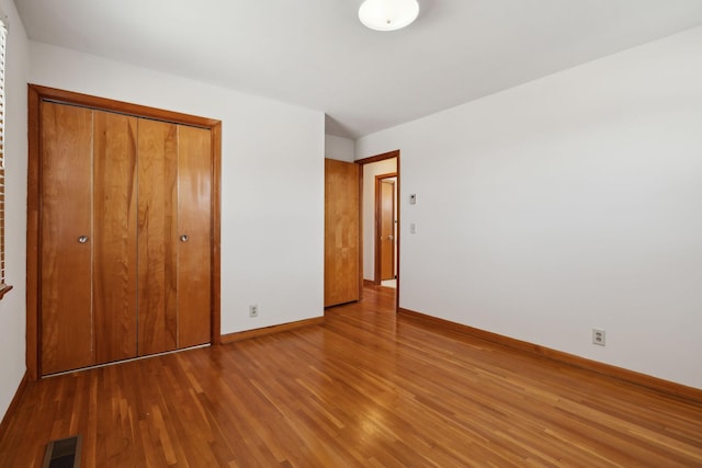 unfurnished bedroom with a closet, visible vents, baseboards, and wood finished floors