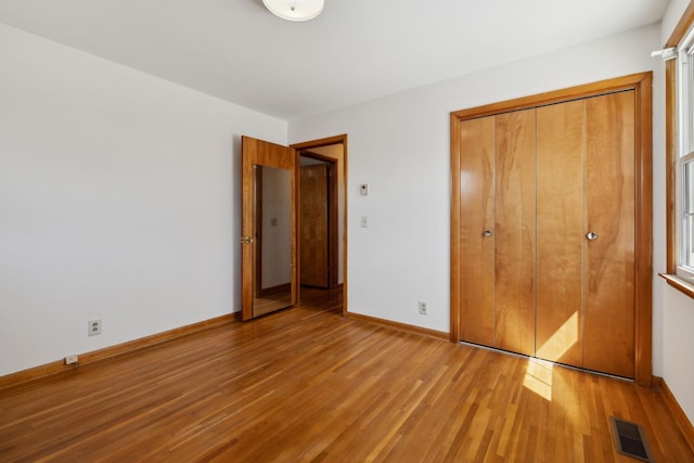 unfurnished bedroom featuring a closet, visible vents, baseboards, and wood finished floors