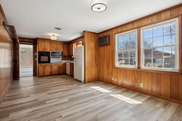 kitchen featuring white appliances, a wall unit AC, brown cabinetry, and light wood-type flooring