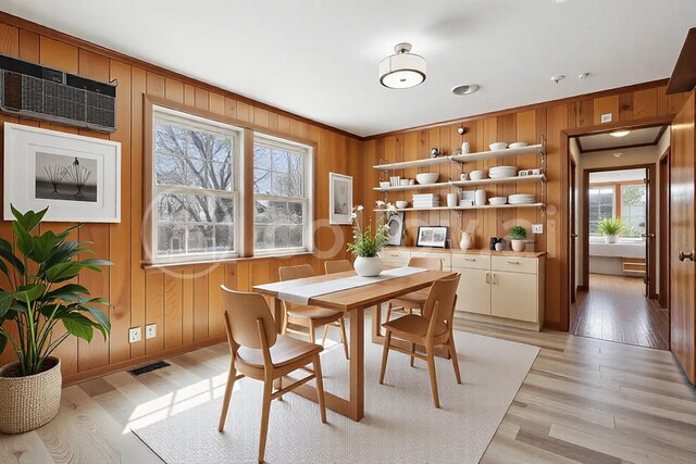 dining room featuring visible vents, baseboards, light wood-style flooring, and wood walls