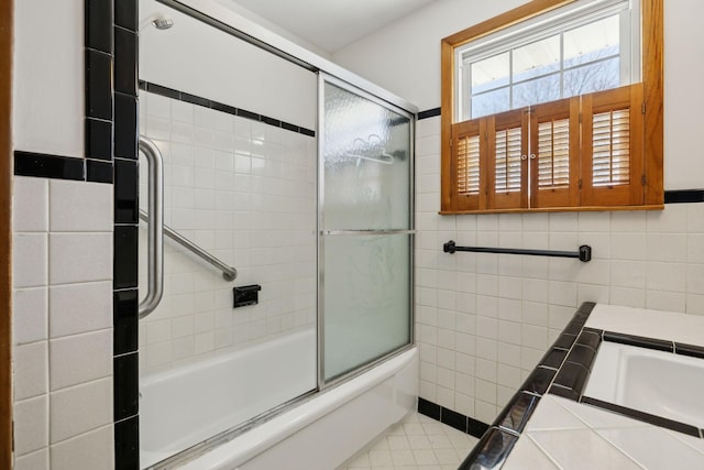 full bath with tile patterned flooring, tile walls, and shower / bath combination with glass door