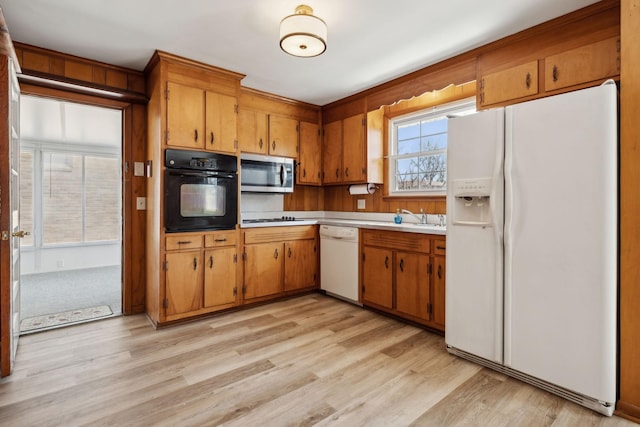 kitchen featuring white appliances, brown cabinetry, light wood-type flooring, and light countertops