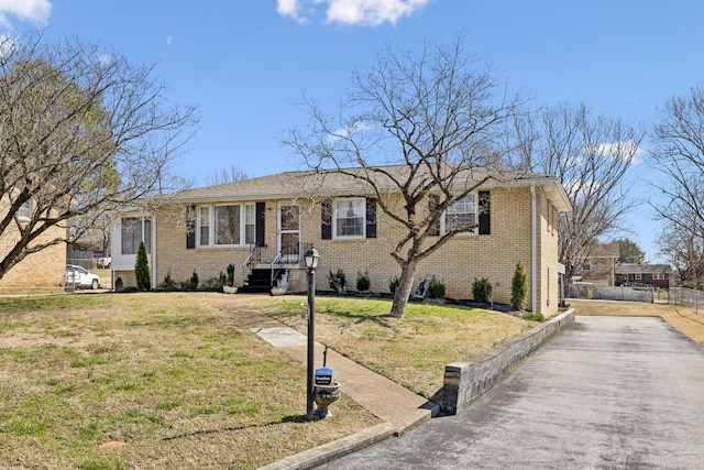 ranch-style home featuring brick siding, a front lawn, and fence