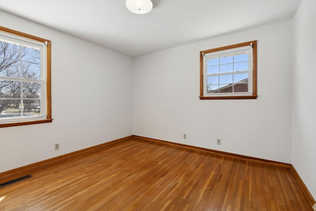 spare room featuring wood finished floors, visible vents, and baseboards