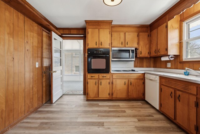 kitchen with wooden walls, a sink, dishwasher, stainless steel microwave, and black oven