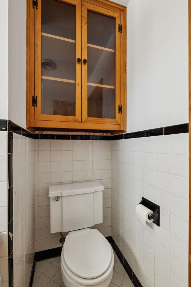 bathroom with tile patterned floors, toilet, tile walls, and a wainscoted wall