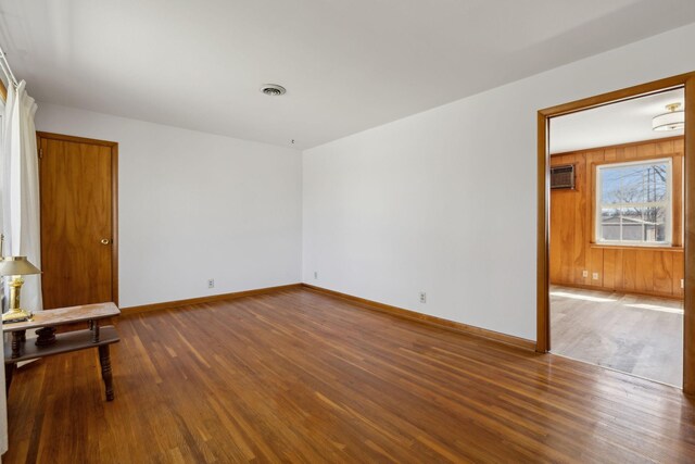 unfurnished room with wooden walls, wood finished floors, visible vents, baseboards, and an AC wall unit