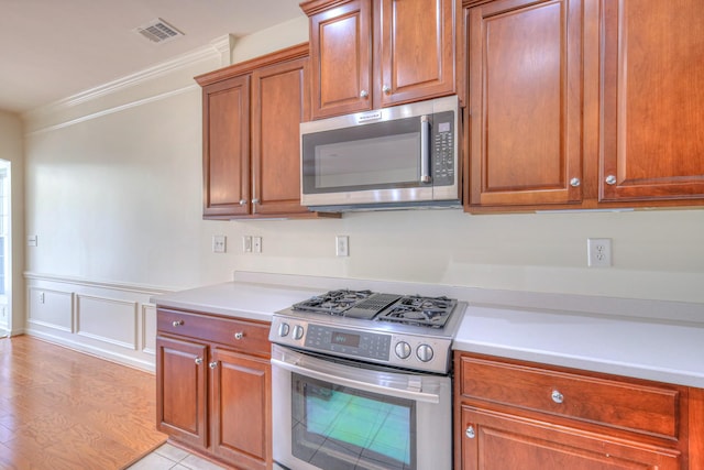 kitchen featuring visible vents, a wainscoted wall, stainless steel appliances, crown molding, and light countertops