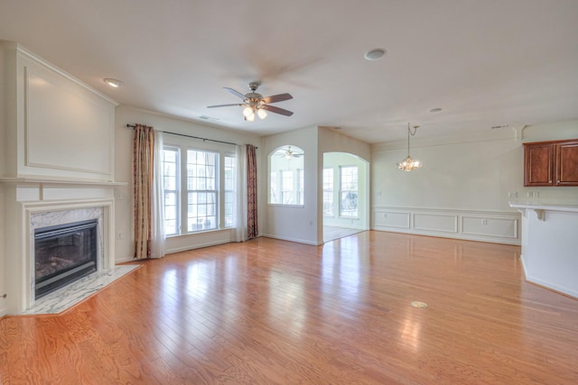 unfurnished living room featuring light wood finished floors, visible vents, ceiling fan with notable chandelier, a fireplace, and arched walkways