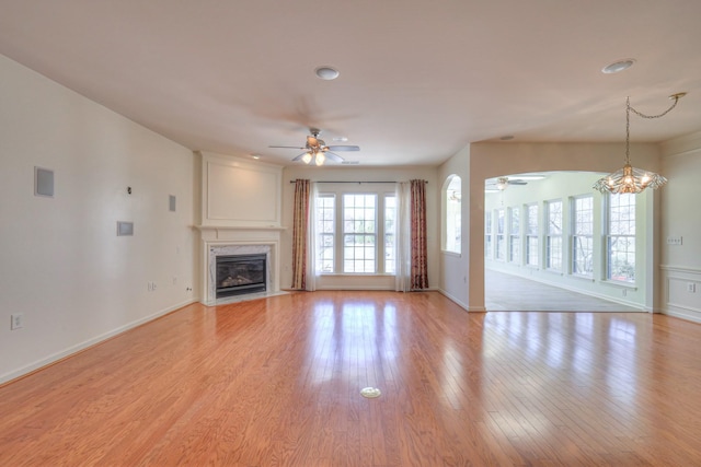 unfurnished living room with light wood-style flooring, ceiling fan with notable chandelier, baseboards, and a high end fireplace