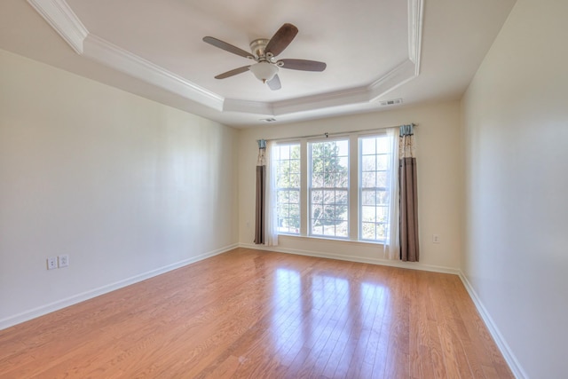 empty room featuring baseboards, visible vents, ornamental molding, light wood-style floors, and a raised ceiling