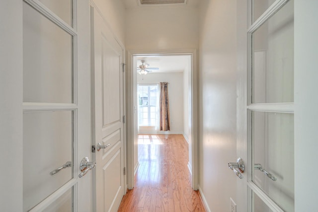 hallway featuring visible vents, light wood-type flooring, and baseboards