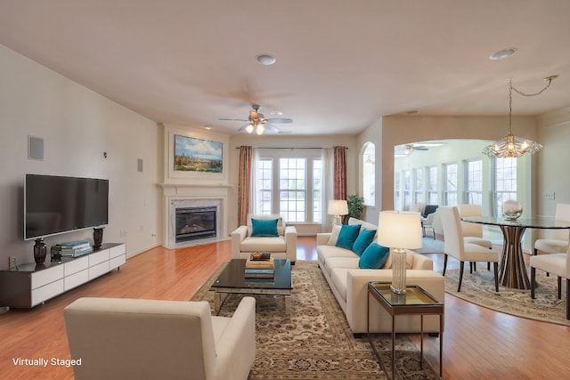 living room featuring visible vents, wood finished floors, a fireplace, and ceiling fan with notable chandelier