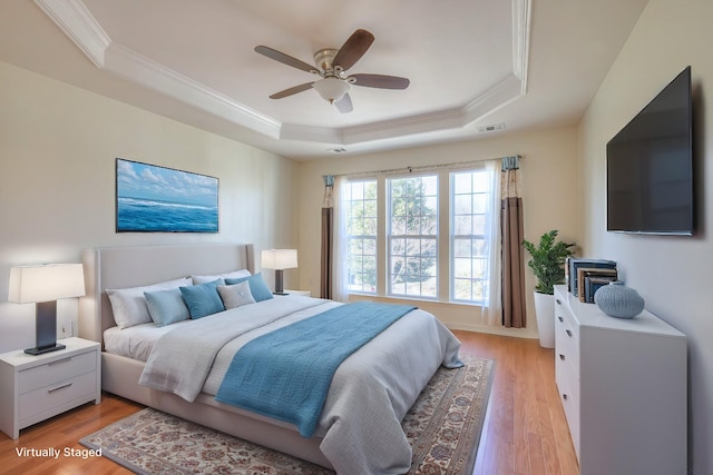 bedroom featuring visible vents, a tray ceiling, light wood-style flooring, ceiling fan, and ornamental molding