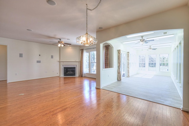 unfurnished living room with a fireplace with flush hearth, ceiling fan with notable chandelier, baseboards, and light wood-style floors