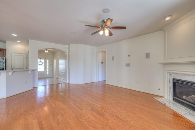 unfurnished living room with a ceiling fan, baseboards, light wood-style flooring, arched walkways, and a high end fireplace