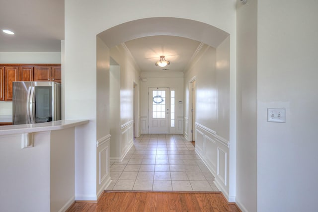 doorway to outside with a wainscoted wall, light tile patterned flooring, arched walkways, ornamental molding, and a decorative wall