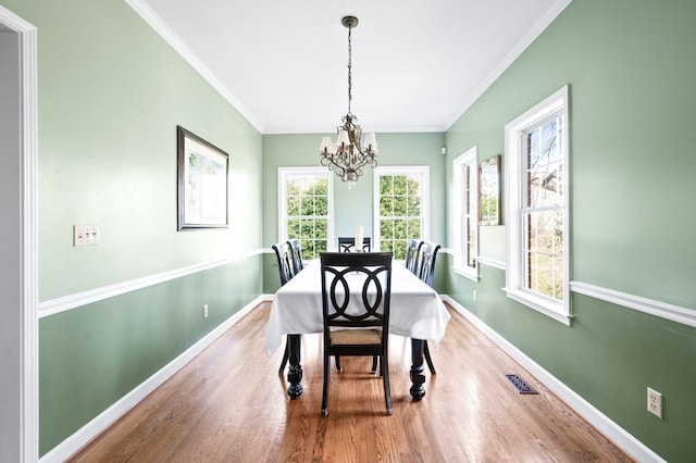 dining room featuring wood finished floors, baseboards, visible vents, ornamental molding, and a chandelier