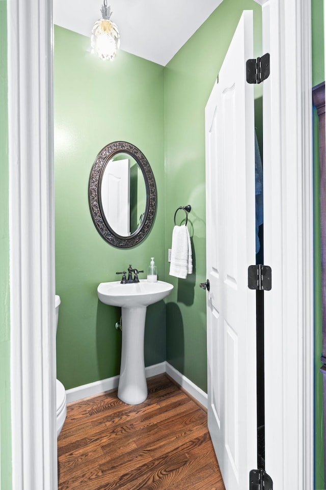 half bath with toilet, wood finished floors, baseboards, and a sink