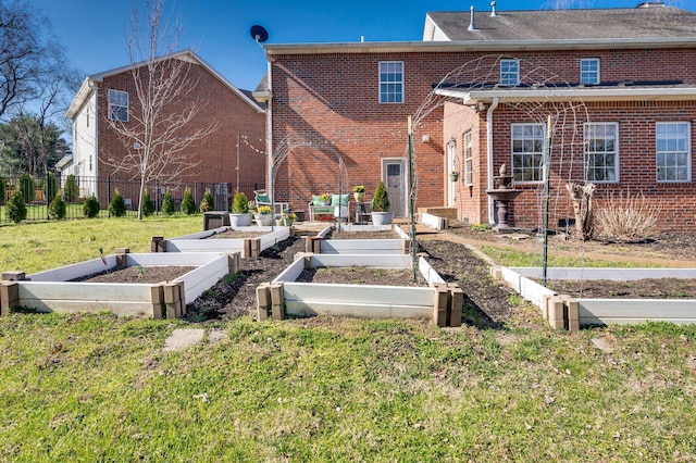 back of house with a vegetable garden, fence, brick siding, and a lawn