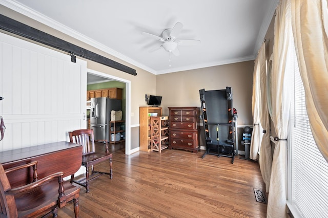 office featuring visible vents, crown molding, a barn door, wood finished floors, and a ceiling fan