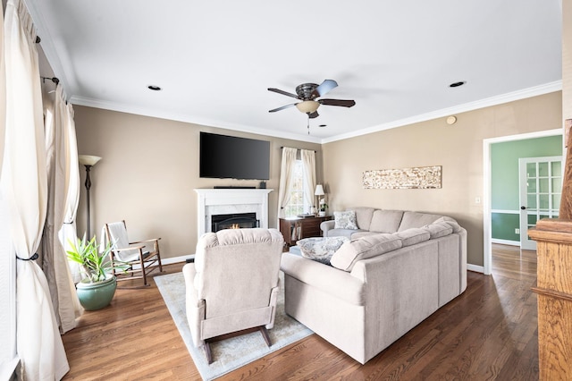 living area with dark wood-type flooring, a fireplace, a ceiling fan, and crown molding