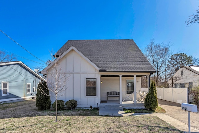 view of front of house with a front lawn, fence, covered porch, board and batten siding, and roof with shingles