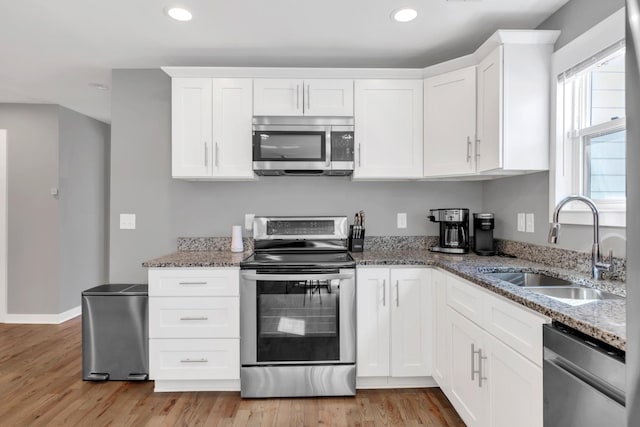 kitchen with a sink, white cabinetry, stone counters, and stainless steel appliances