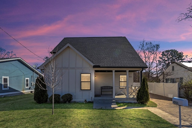 view of front facade with board and batten siding, fence, a porch, roof with shingles, and a lawn