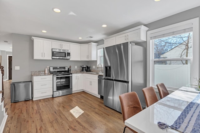 kitchen with light stone counters, a sink, light wood-style floors, appliances with stainless steel finishes, and white cabinetry