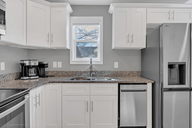 kitchen with a sink, stainless steel appliances, light stone countertops, and white cabinetry