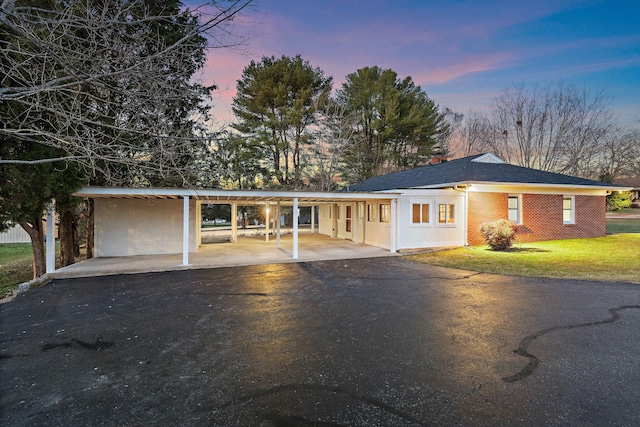 view of front facade featuring brick siding, an attached carport, driveway, and a front lawn