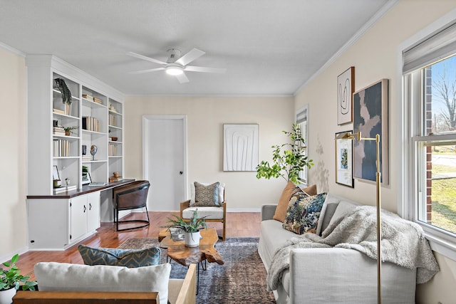 living area with a ceiling fan, wood finished floors, crown molding, baseboards, and built in study area