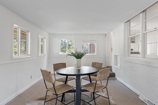 tiled dining room featuring visible vents and brick wall