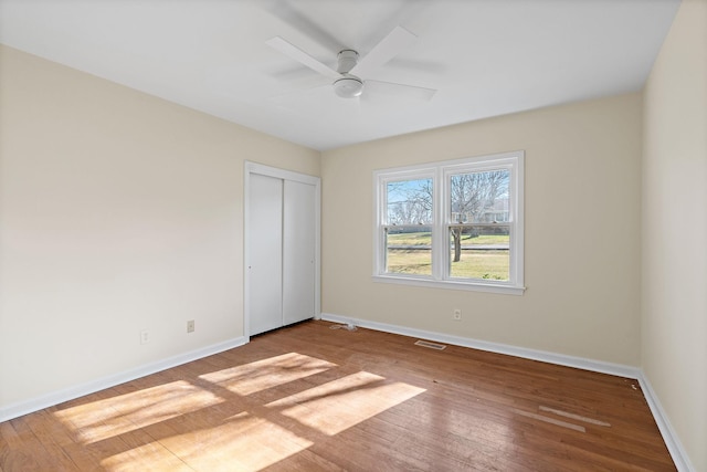 unfurnished bedroom featuring visible vents, baseboards, a closet, a ceiling fan, and wood-type flooring