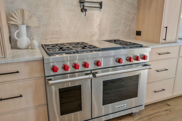 kitchen featuring double oven range, light stone countertops, backsplash, and light brown cabinetry