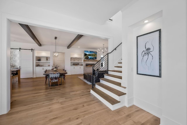 interior space with beamed ceiling, wood finished floors, a barn door, a lit fireplace, and a chandelier