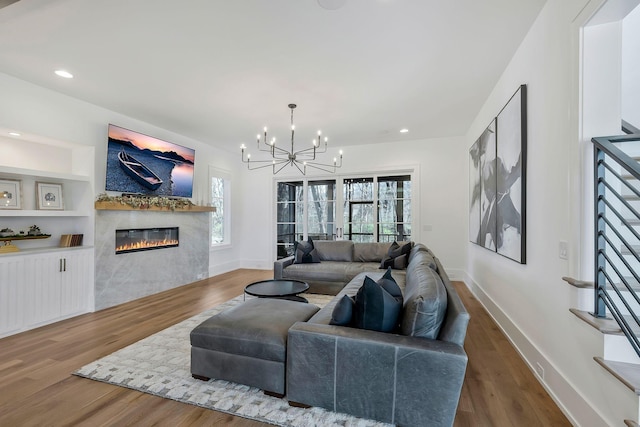 living area with a glass covered fireplace, wood finished floors, baseboards, and a chandelier