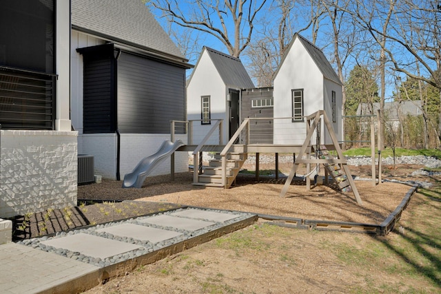 rear view of property featuring central AC unit, a playground, and roof with shingles