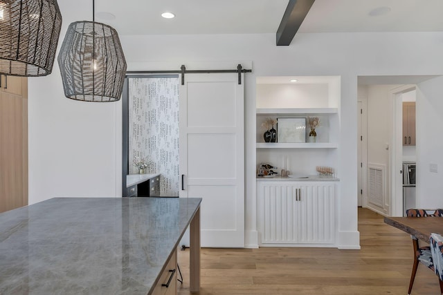 kitchen with light stone countertops, visible vents, a barn door, beamed ceiling, and light wood-type flooring