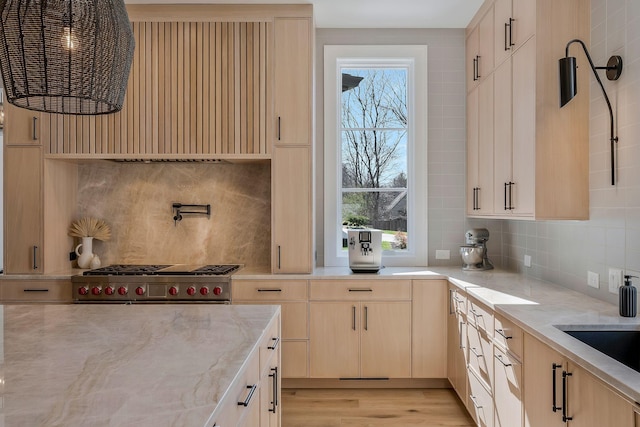 kitchen featuring light stone counters, plenty of natural light, light brown cabinetry, and stainless steel range