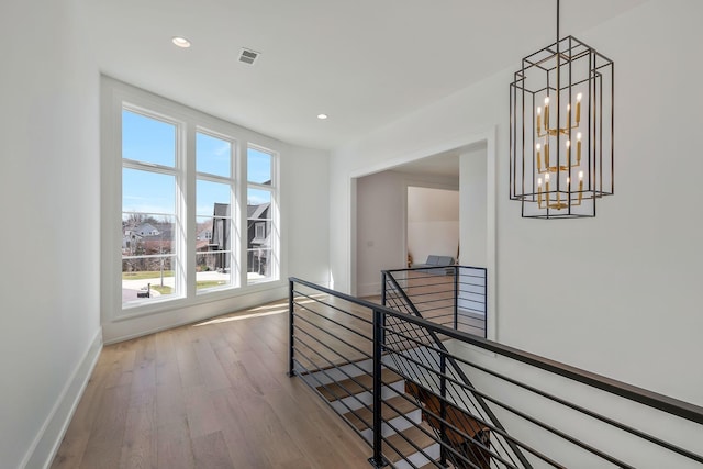 hallway with wood finished floors, visible vents, baseboards, recessed lighting, and an upstairs landing