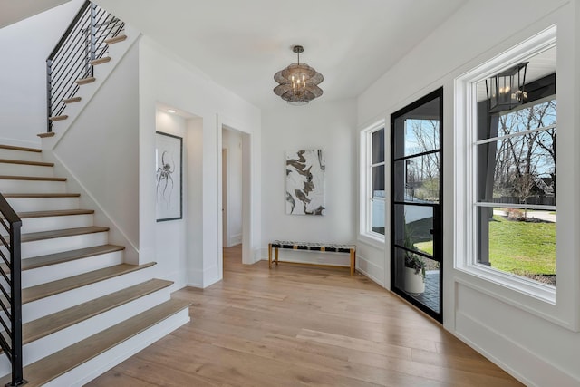 entrance foyer featuring plenty of natural light, light wood-style flooring, stairway, and an inviting chandelier