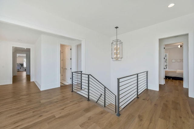 hallway featuring light wood-type flooring, an upstairs landing, a notable chandelier, recessed lighting, and baseboards