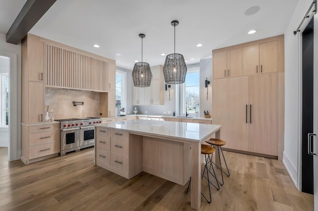 kitchen featuring light brown cabinets, a barn door, range with two ovens, a kitchen breakfast bar, and light wood-style floors