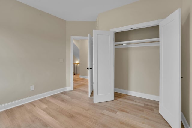 unfurnished bedroom featuring light wood-type flooring, baseboards, and a closet