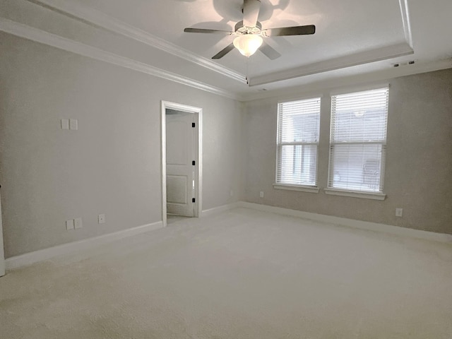 empty room with light colored carpet, a raised ceiling, baseboards, and ornamental molding