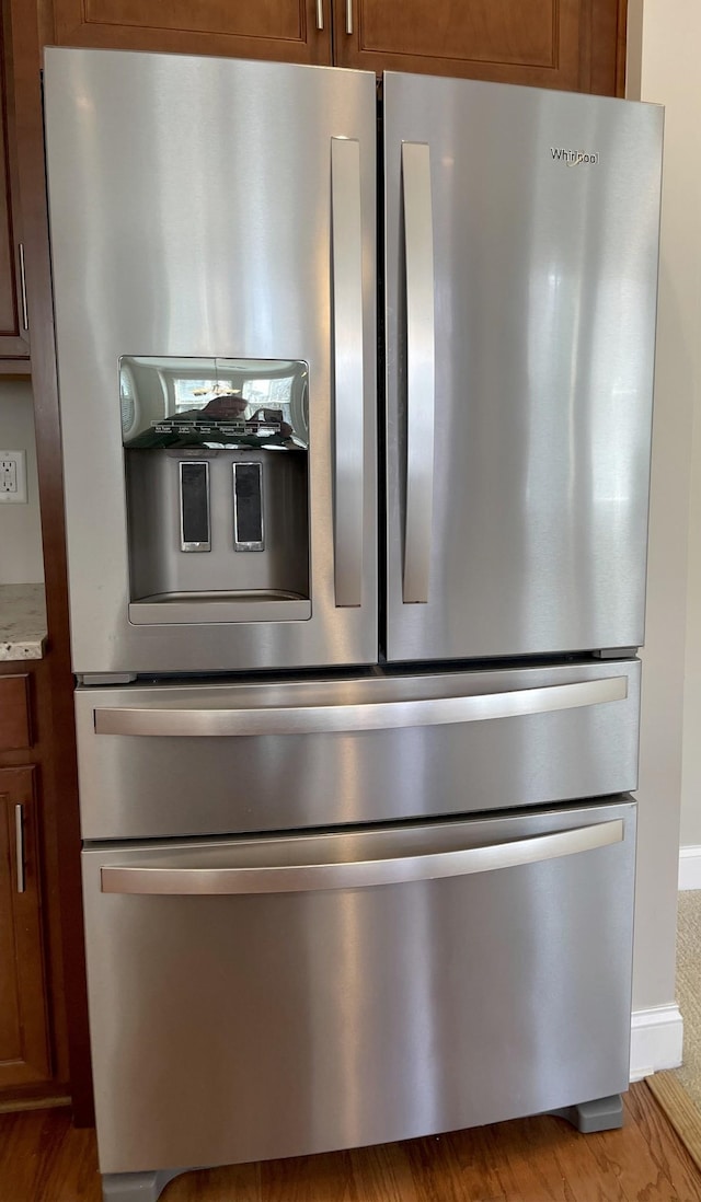 interior details with stainless steel fridge, light stone countertops, brown cabinets, and wood finished floors