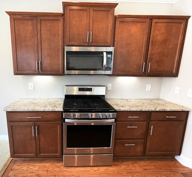 kitchen with light stone counters, appliances with stainless steel finishes, and wood finished floors